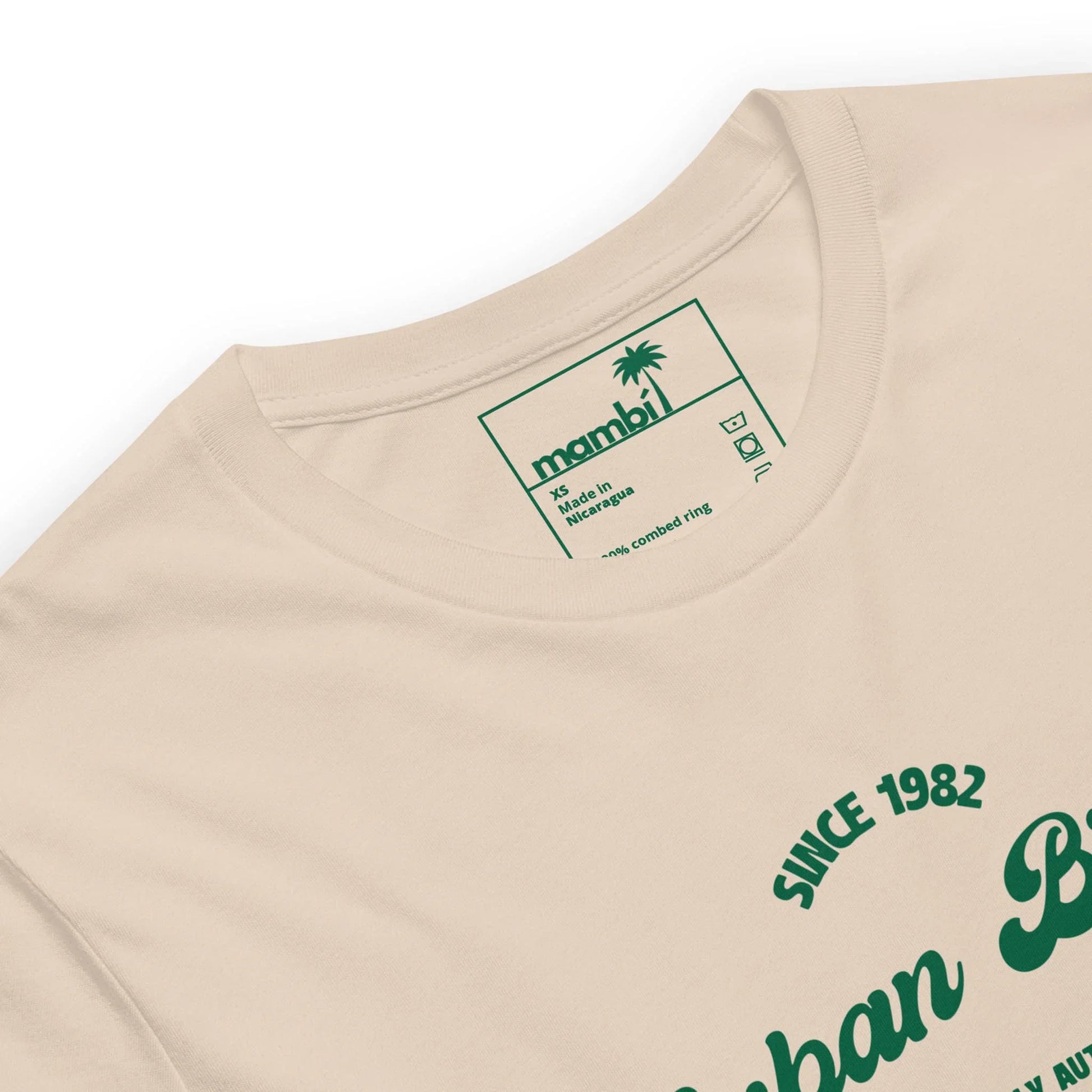 A close-up of the Cuban Bros Graphic Tee from Printful, a beige unisex t-shirt with green chest text and an inner collar label showing a palm tree, Printful branding, size XL, and washing instructions.