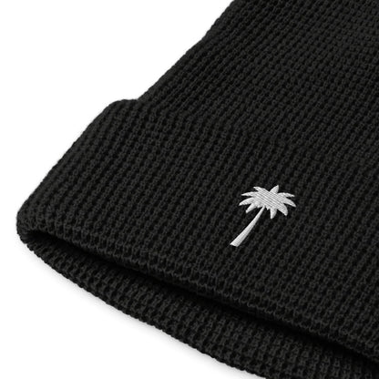 Close-up of a black knitted Mambí beanie featuring a small white palm tree embroidered on the folded cuff.