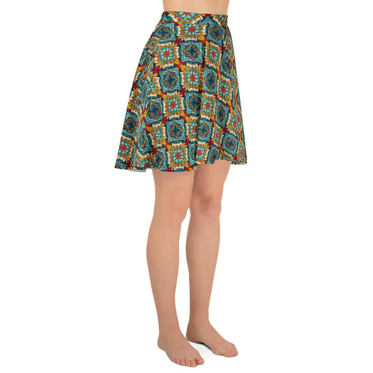 A person stands barefoot in the Printful Dinorah Skater Skirt for women, featuring a knee-length, colorful geometric print in orange, blue, and green tones. The elastic waistband ensures a flattering fit. Upper body not visible.