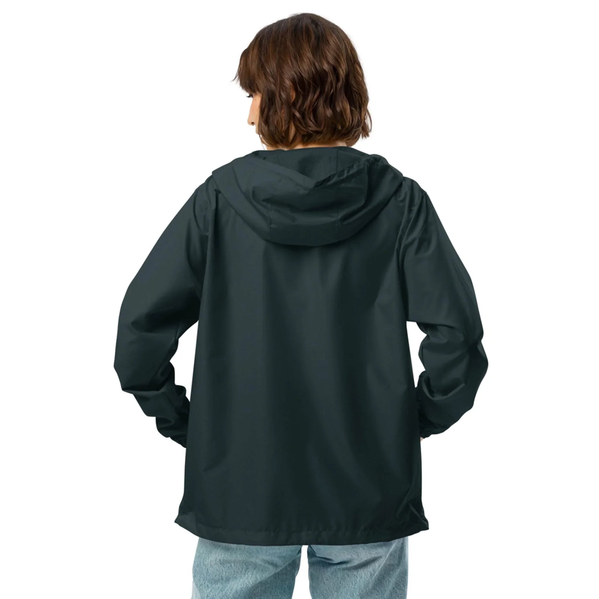 A person with short brown hair, wearing a dark Mambí hooded jacket and light blue jeans, stands with their back to the camera against a plain white background.