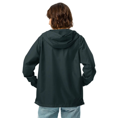 A person with short brown hair, wearing a dark Mambí hooded jacket and light blue jeans, stands with their back to the camera against a plain white background.