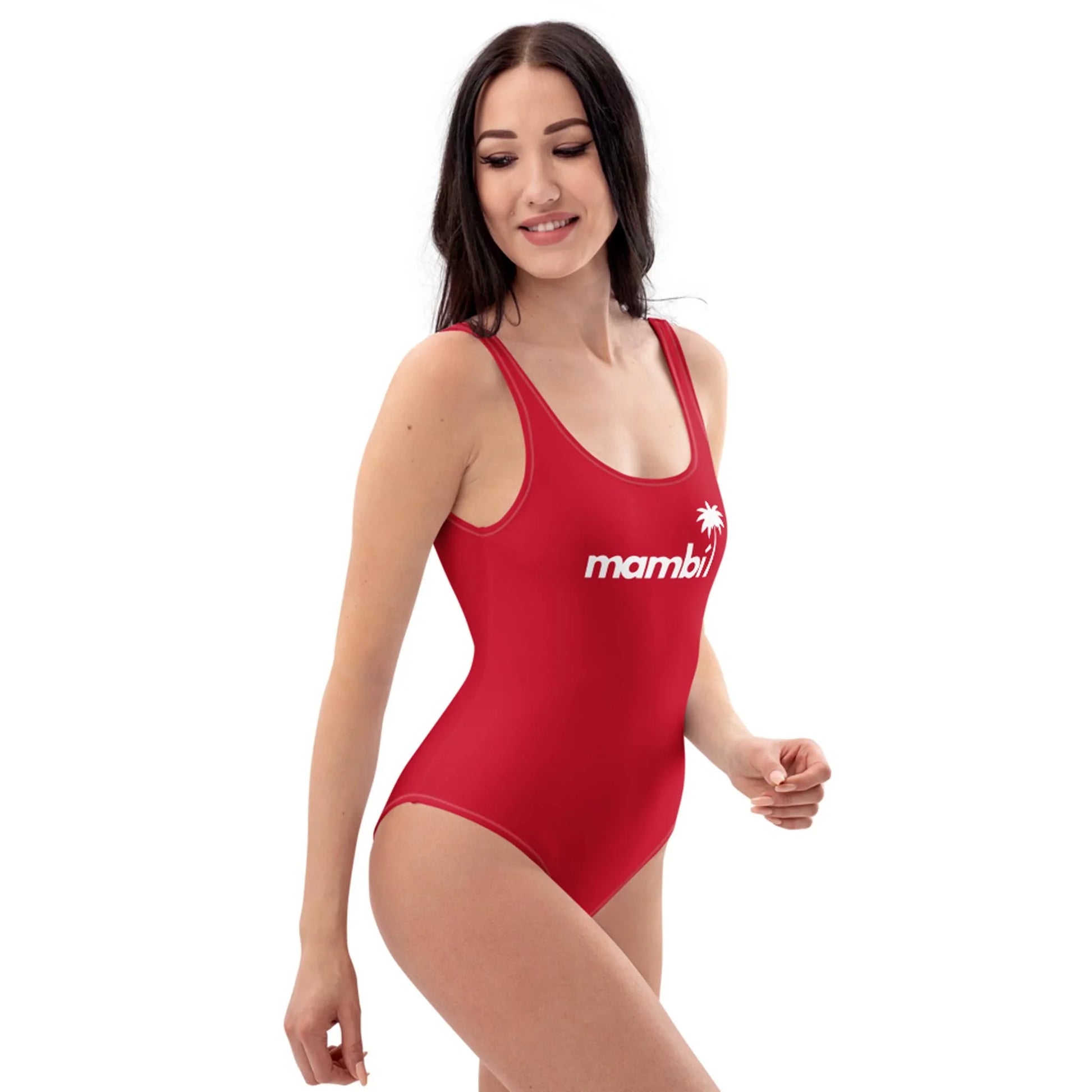 A woman with long dark hair wears a red one-piece swimsuit with Mambí and a small palm tree graphic on the front. She is smiling and looking to the side against a plain white background.