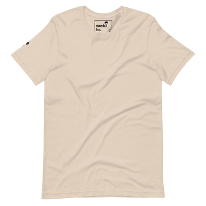 A plain beige Mambí t-shirt with a small black palm tree logo on the left sleeve and a visible black and white neck tag, laid flat against a white background.