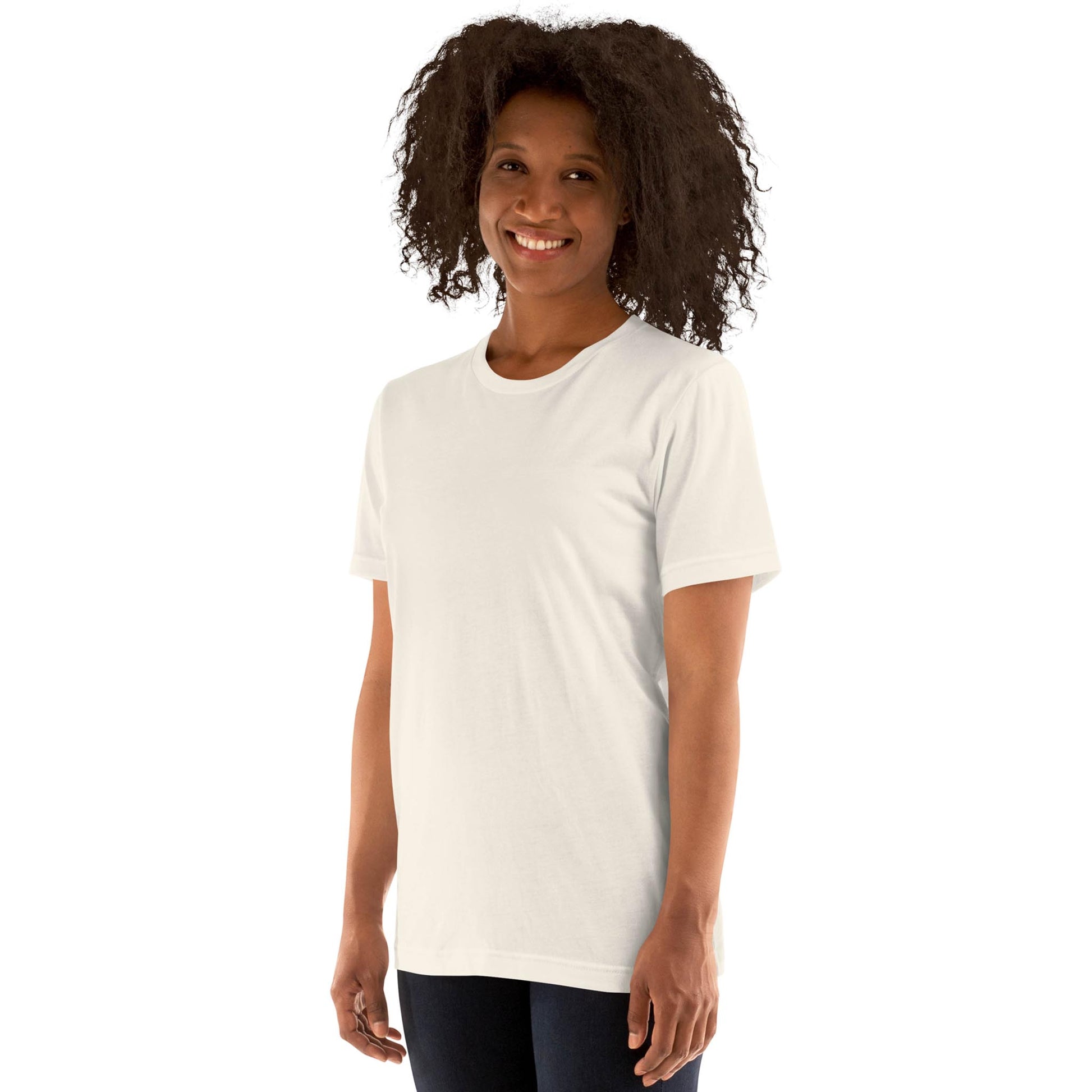 A person with curly hair smiles while standing in a plain white Mambí short-sleeve t-shirt and dark pants against a white background.