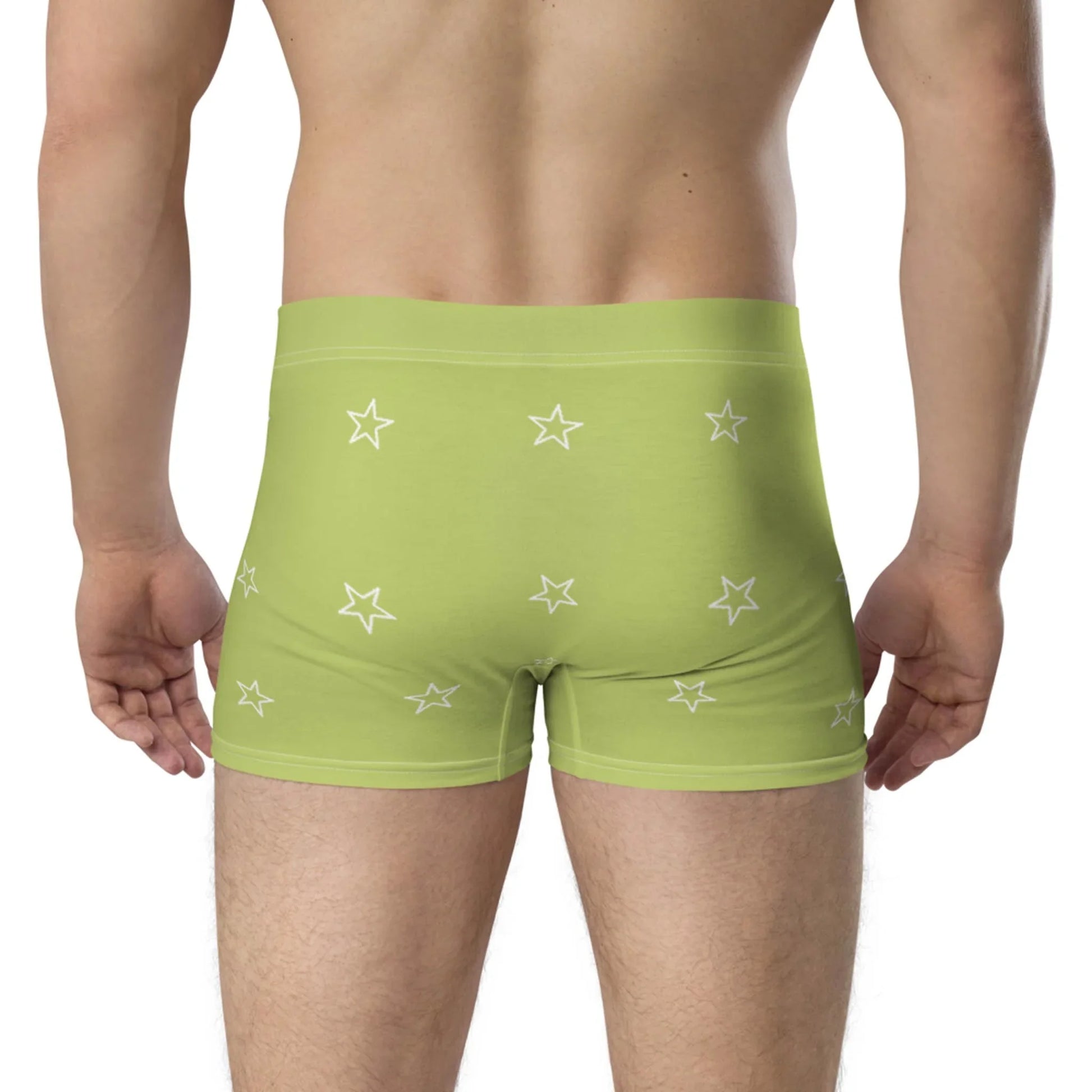 A person is shown from the waist down, wearing light green Mambí boxer briefs with a pattern of white stars. They are standing with their back to the camera against a plain white background.