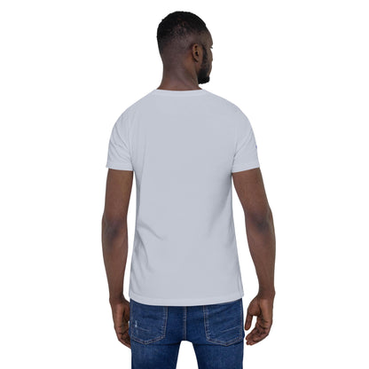 A man is standing with his back to the camera, wearing a plain light gray short-sleeve Mambí t-shirt and blue jeans against a white background.
