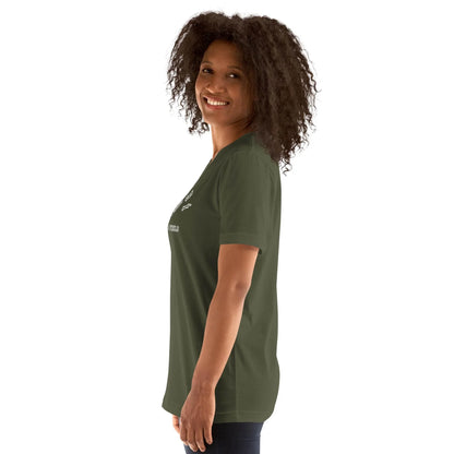 Woman with curly hair smiling and standing sideways, wearing a dark green Mambí t-shirt and dark pants against a plain white background.