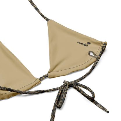 Close-up of the Flavia String Bikini Swimsuit by Printful, featuring tan recycled polyester, black and brown animal print straps, a “mambi” logo, and a small palm tree graphic.