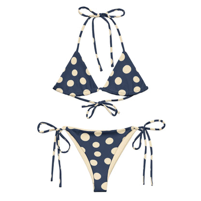 A navy blue Mambí bikini with large cream-colored polka dots. The top features a triangle style with halter and back ties, while the bottoms have adjustable side ties.