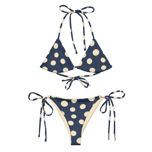 A navy blue Mambí bikini with large cream-colored polka dots. The top features a triangle style with halter and back ties, while the bottoms have adjustable side ties.