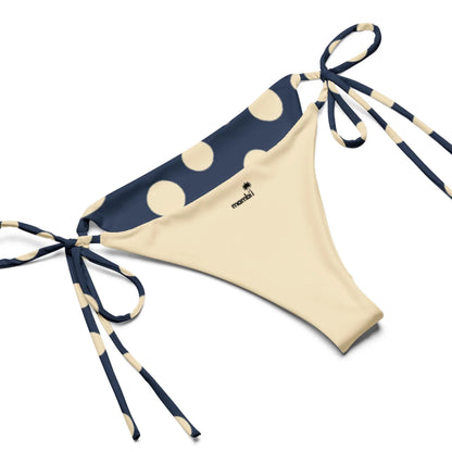 Beige bikini bottom with navy blue waistband and side ties, decorated with large cream polka dots. The brand name monini and a subtle Mambí accent appear near the waistband.