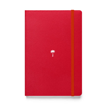 A red Mambí notebook featuring a small white palm tree illustration in the center of the cover and an orange elastic band on the right side for closure.