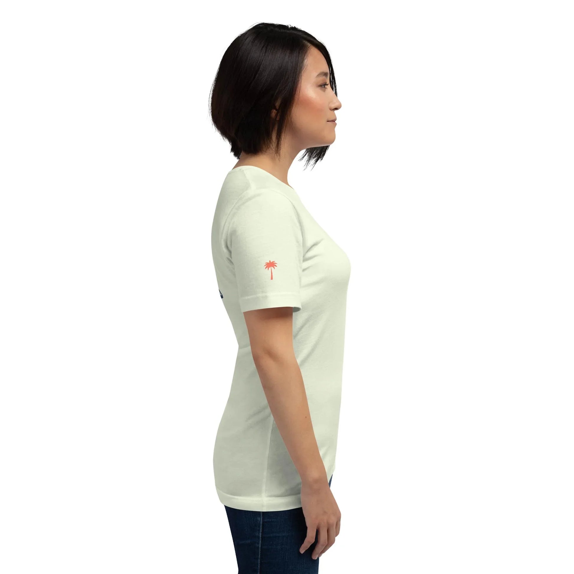 A woman with short dark hair stands in profile, wearing the Printful Knowledge Graphic Tee and dark jeans against a plain white background.