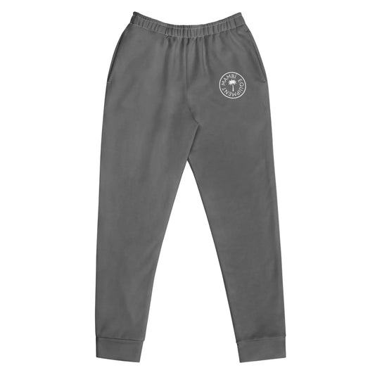 Gray jogger sweatpants with an elastic waistband, side pockets, cuffed ankles, and a small white circular Mambí logo on the left upper thigh. The joggers are laid flat on a white background.