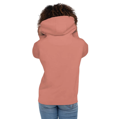 A person with curly hair, seen from behind, wears a rose-colored Mambí hoodie and blue jeans. The hood is up, partially covering their head and shoulders.