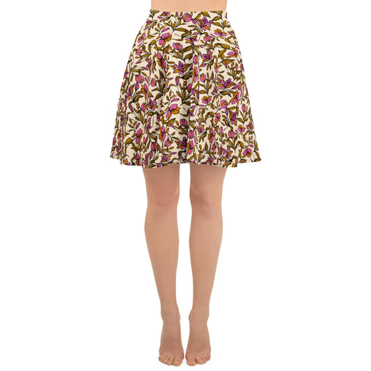 A person wearing a knee-length, pleated skirt with a colorful Mambí floral pattern on a white background stands barefoot against a plain white backdrop.