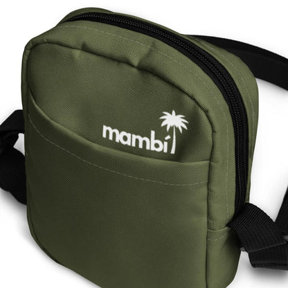 Close-up of a small olive green Mambí fabric bag with a front pocket, black zipper, and adjustable black strap. The word Mambí and a palm tree logo are printed in white on the front.