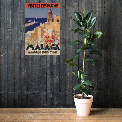 A tall potted rubber plant stands on a wooden floor in front of a dark wooden wall, next to a vintage-style Mambí travel poster for Malaga, Spain.