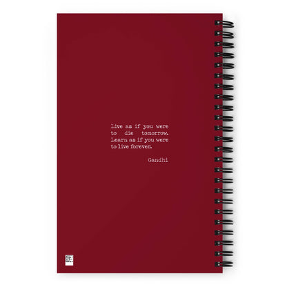 A maroon custom wire-bound notebook with dotted pages, featuring a centered white quote: Live as if you were to die tomorrow. Learn as if you were to live forever. - Gandhi. The background is plain with no other designs.