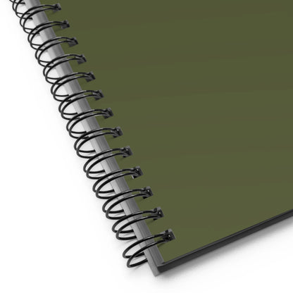Close-up of the corner of a custom wire-bound notebook with a dark green cover, showing the black metal binding and part of the pages beneath.