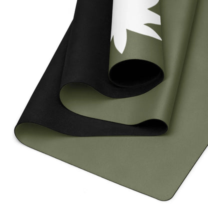 A close-up of a rolled, two-tone Mambí yoga mat with an olive green top layer featuring a white leaf design and a black underside. The edges and texture of the mat are clearly visible.