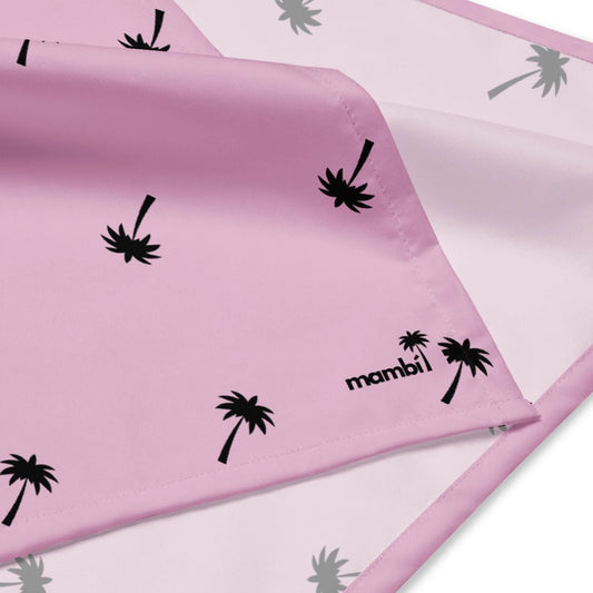 A pink satin fabric with black palm tree prints and Mambí in black text in the corner. The fabric has stitched edges and is partially folded to reveal both sides.