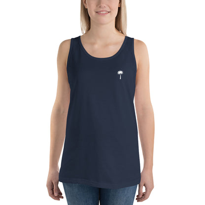 A woman wearing a sleeveless navy blue classic tank top made from ringspun cotton, featuring a small white palm tree graphic on the left chest, paired with blue jeans. She is smiling and facing forward.