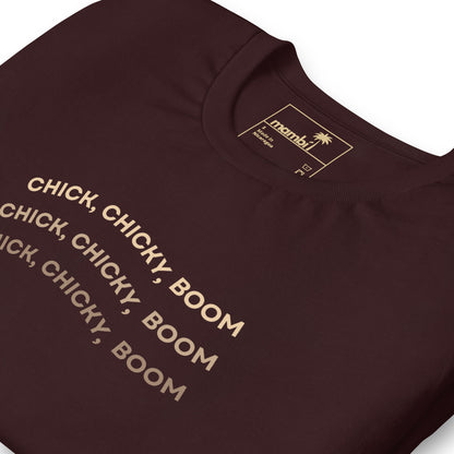 A maroon fitted shirt with the text CHICK, CHICKY, BOOM repeated three times in bold, beige letters. This comfortable cotton tee from Manby features graphic tees style and includes care information on the label.