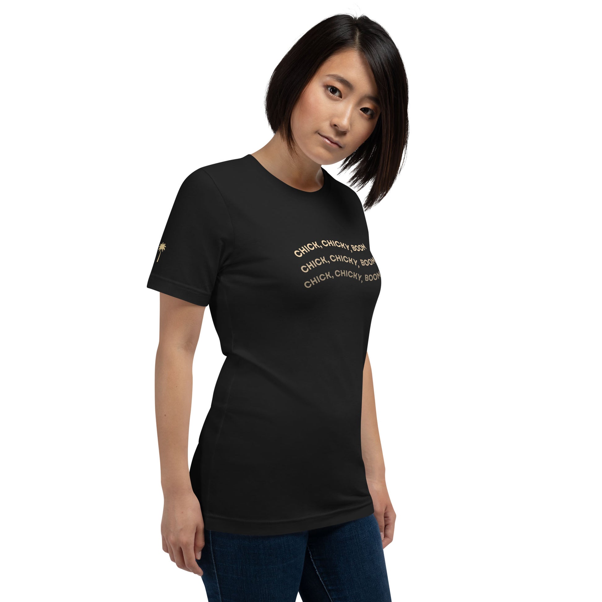 A woman with straight, shoulder-length hair wears a comfortable cotton graphic tee with gold text that reads, CHICK, CHICKY, BOOM multiple times. She stands against a plain white background, looking slightly to the side.