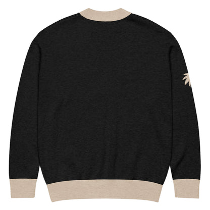 A black two-tone cardigan with beige cuffs, collar, and waistband. There is a small beige palm tree design on the right sleeve near the shoulder. The jacquard knit cardigan is shown from the back.