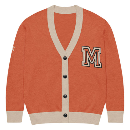 A burnt orange & taupe unisex cardigan with beige trim, black buttons, and a bold black-outlined M patch on the upper left. The upper right sleeve features a small white accent for standout style.