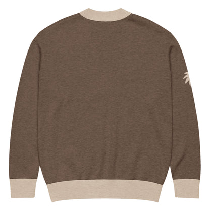A brown jacquard knit sweater with beige ribbed cuffs, collar, and hem, shown from the back. A small beige palm tree design accents the upper part of the left sleeve.