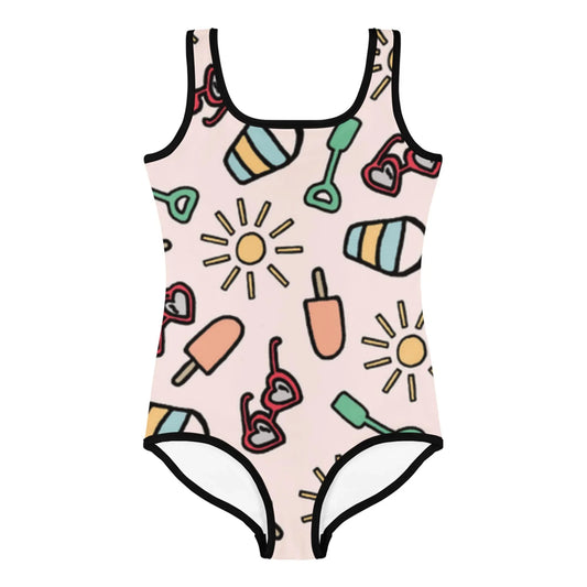 A one-piece swimsuit by Mambí with a light pink background featuring playful illustrations of suns, popsicles, heart-shaped sunglasses, beach balls, and green shovels, all outlined in black.