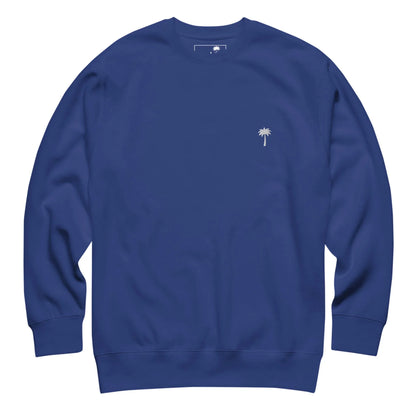 A plain blue crewneck sweatshirt featuring a small white palm tree emblem on the left chest, inspired by Mambí style.