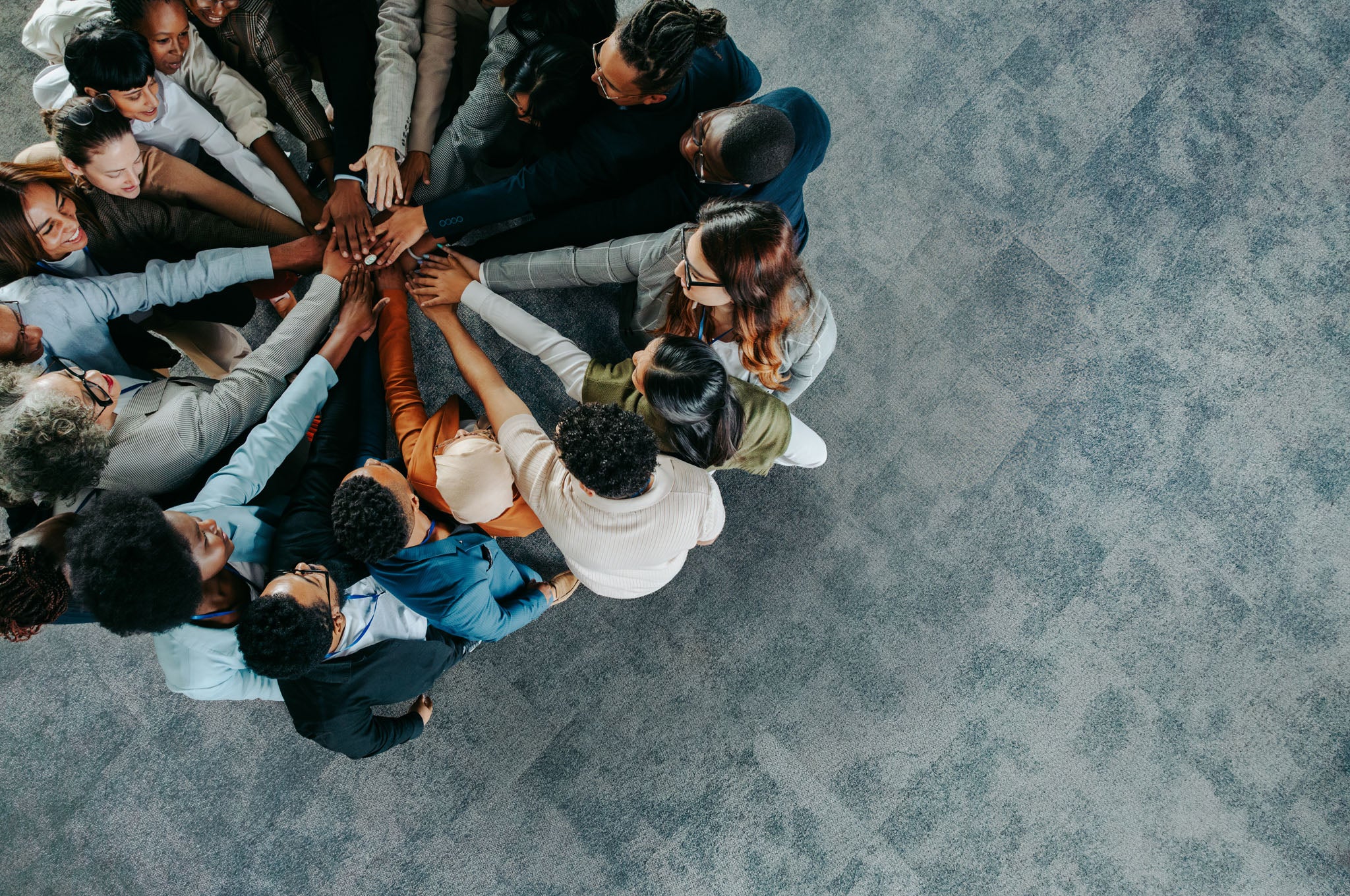 Group of people with their hands together in a circle on a gray pavement.