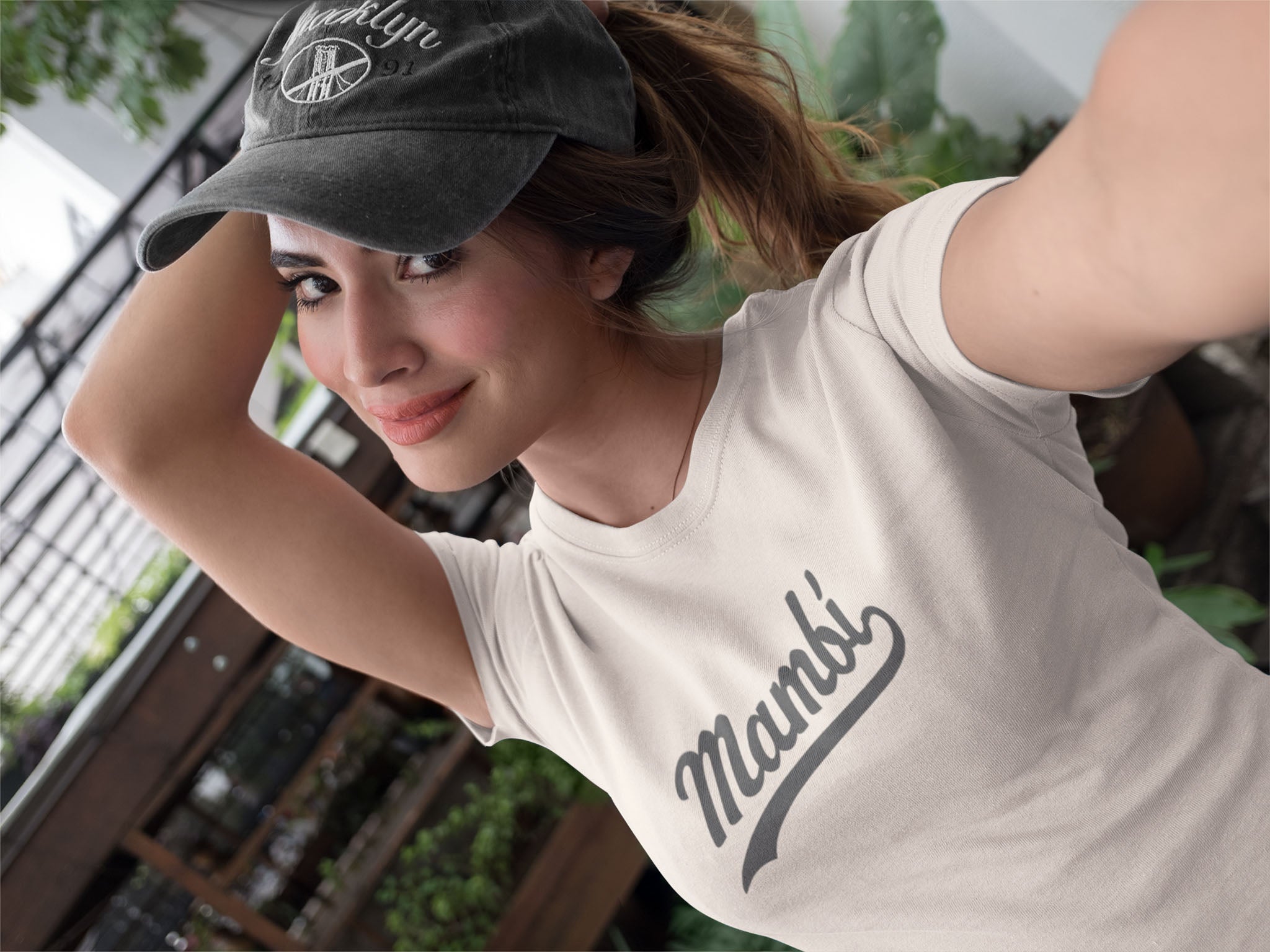 Woman wearing a cap and a 'Mambi' t-shirt with a blurred outdoor background