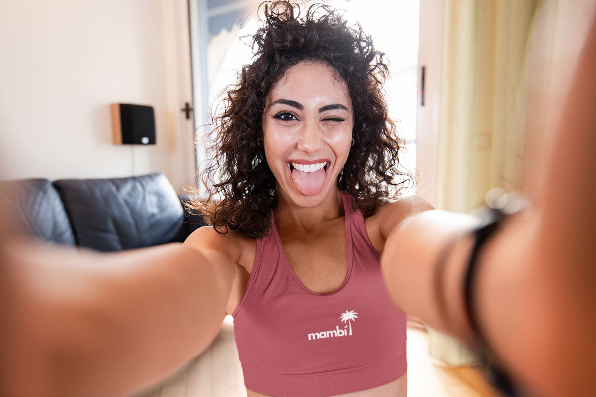 Woman taking a selfie in a pink sports bra with a mambi palm tree logo design, indoors.