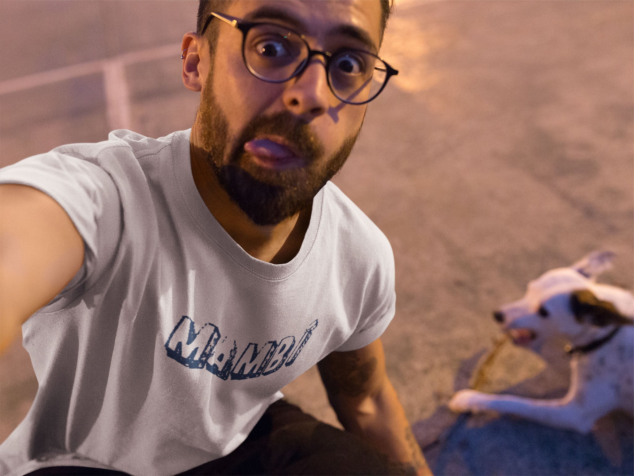 Man wearing a white t-shirt with 'mambi' printed on it, sitting next to a dog.