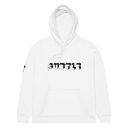 A white hoodie with a front pocket features the word SUBTLE in bold, black and white block letters on the chest, inspired by Mambí style. A small black palm tree graphic accents the left sleeve.