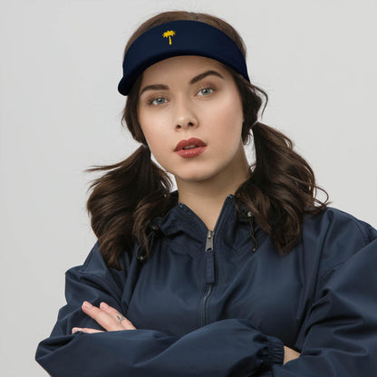 A woman with dark brown hair in pigtails wears a navy visor featuring a small yellow palm tree emblem and a matching Mambí navy jacket, standing with folded arms against a plain light background.